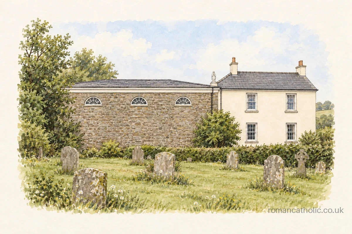 Plain stone chapel with three high lunette windows beside a cream house, seen across a graveyard.